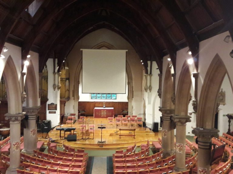Interior of a church with seating, altar, and projector screen in a gothic style.