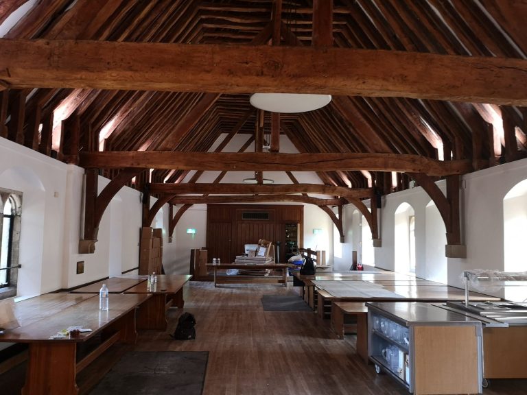 Spacious interior of a room with wooden beams and large tables, under soft natural light.