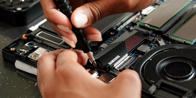 Hands using a tool to repair or assemble a laptop's internal components.